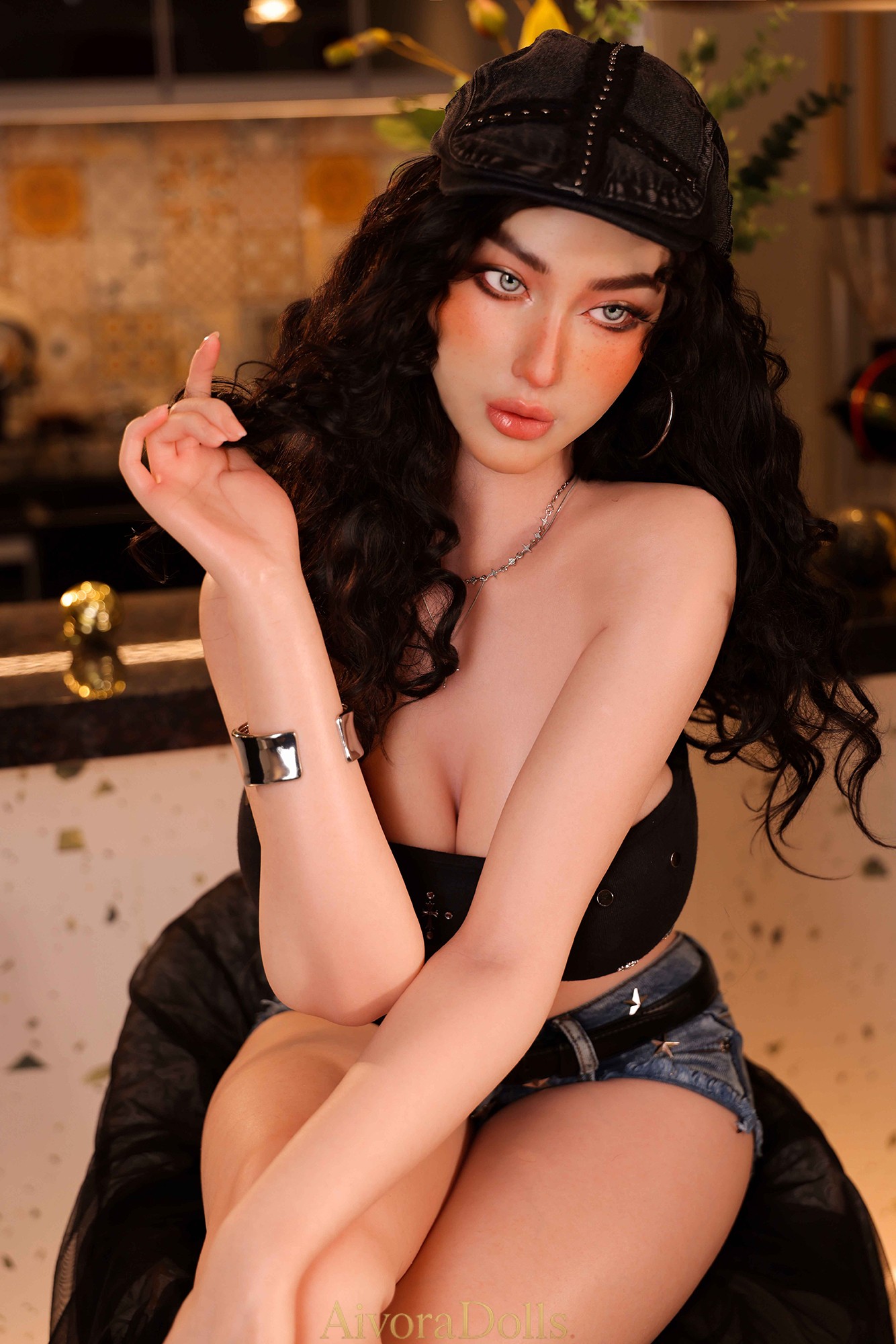 Silicone doll with black curls wearing a black cap, studded bandeau top, frayed denim shorts and pointed black boots beside a counter.